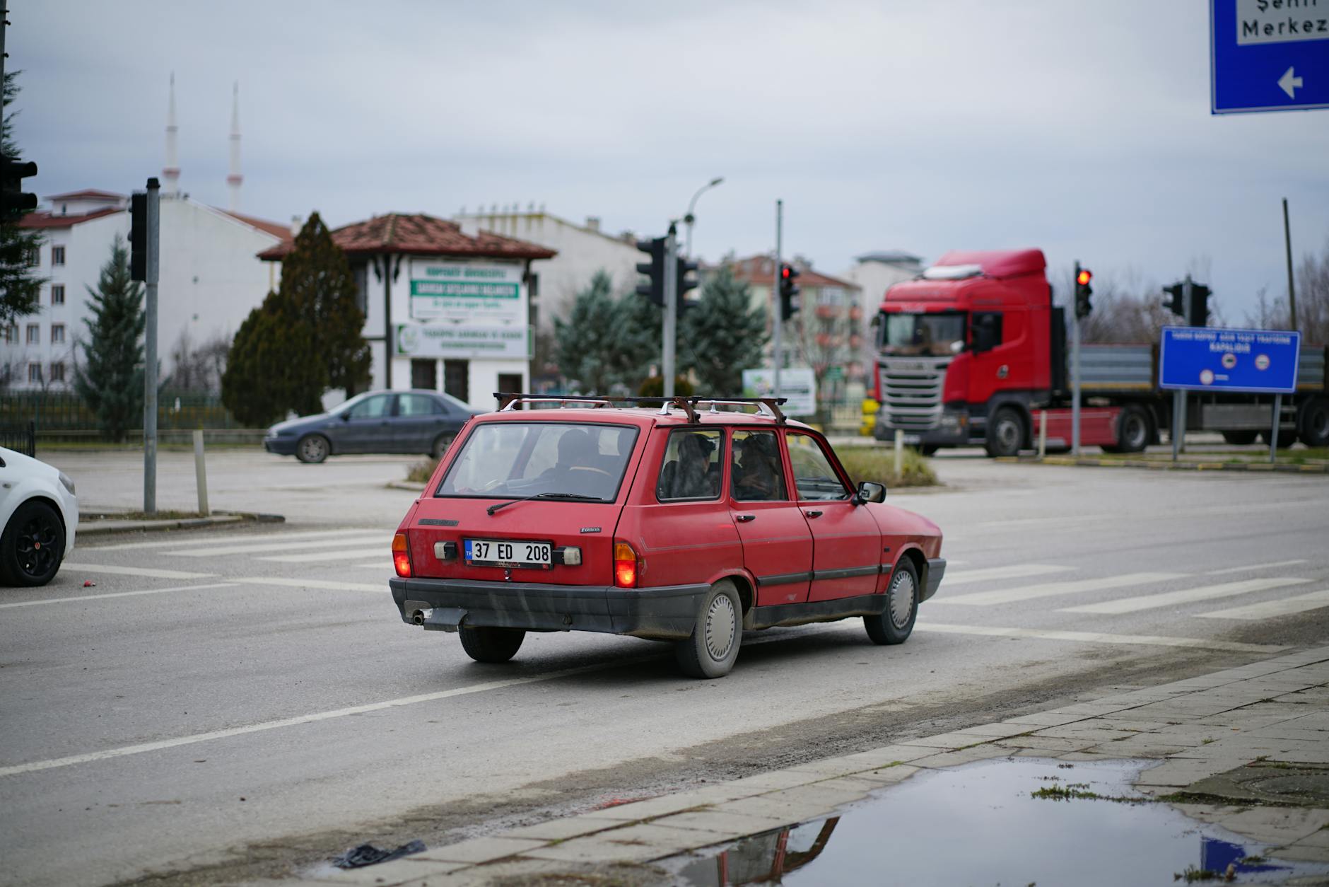 Czerwony Fiat 126p jedzie ulicą miasta z znakami drogowymi w tle