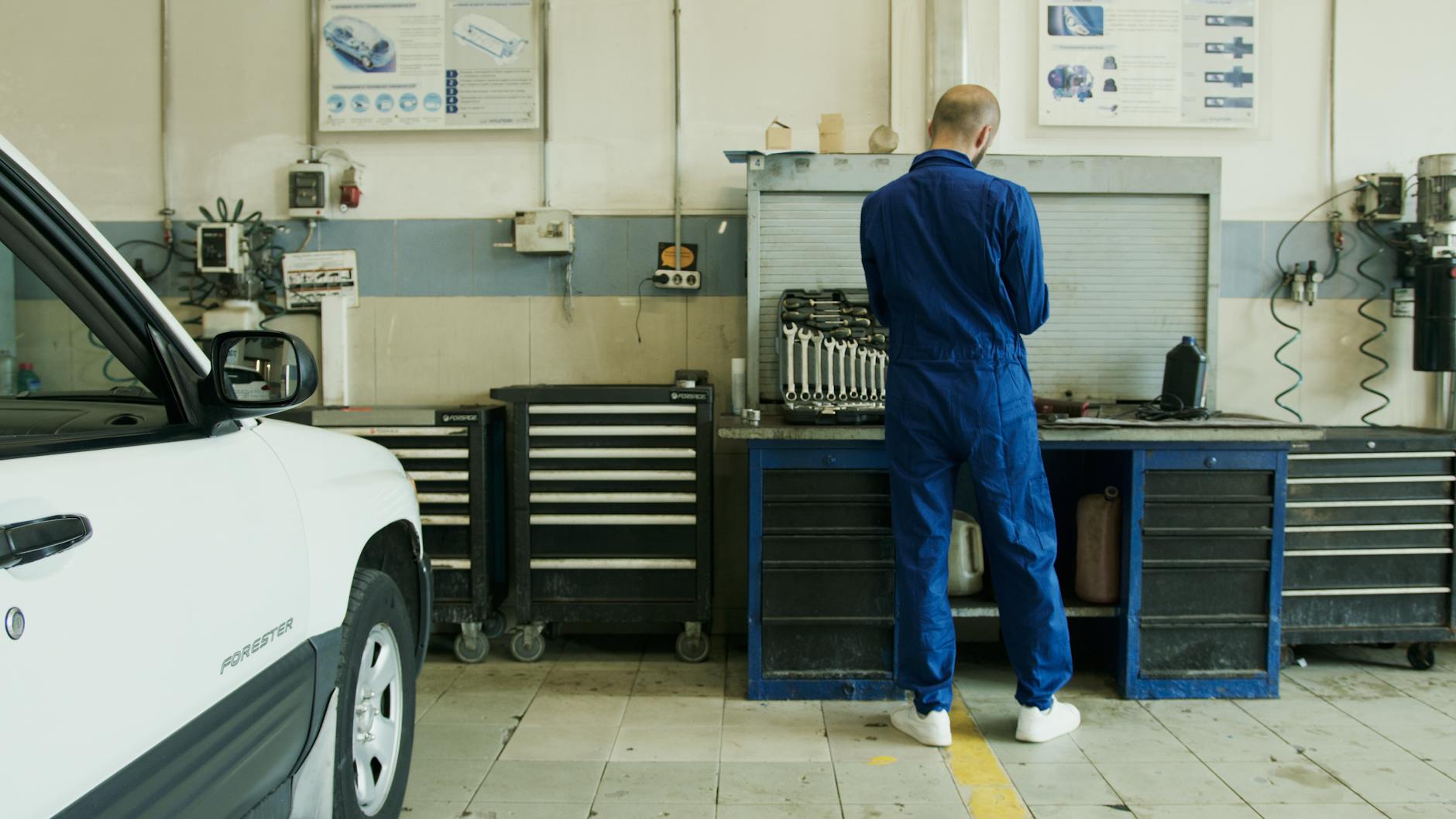 Mechanik w niebieskim kombinezonie sprawdza białe Mitsubishi w warsztacie