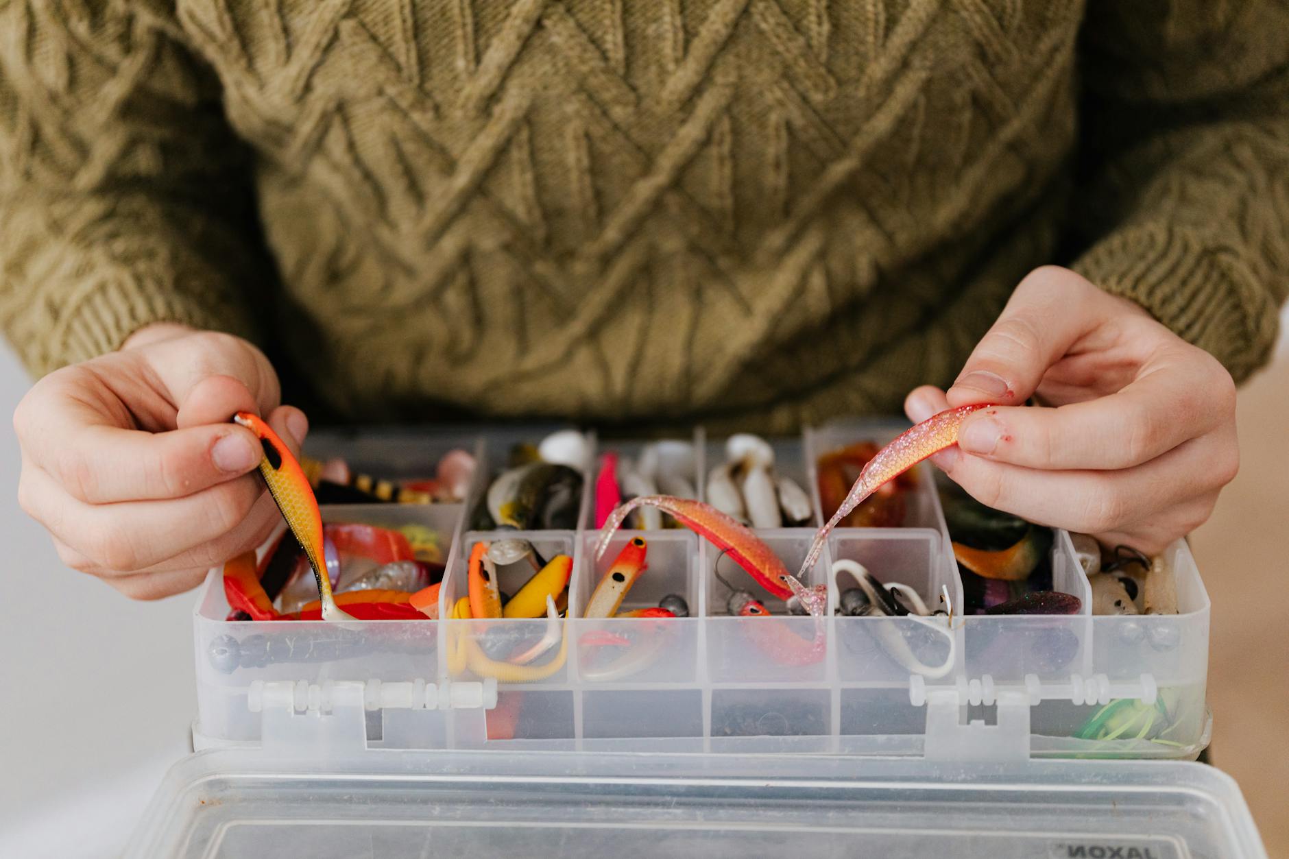 Ręce wędkarza układają kolorowe przynęty w pudełku tackle box