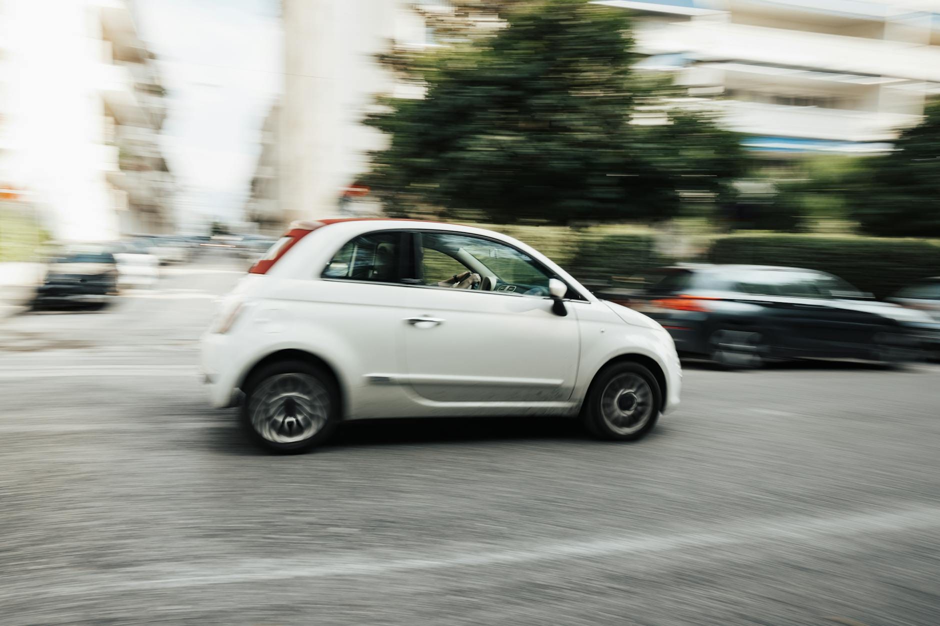 Biała Mazda 2 jedzie szybko po miejskiej ulicy z efektem rozmycia ruchu