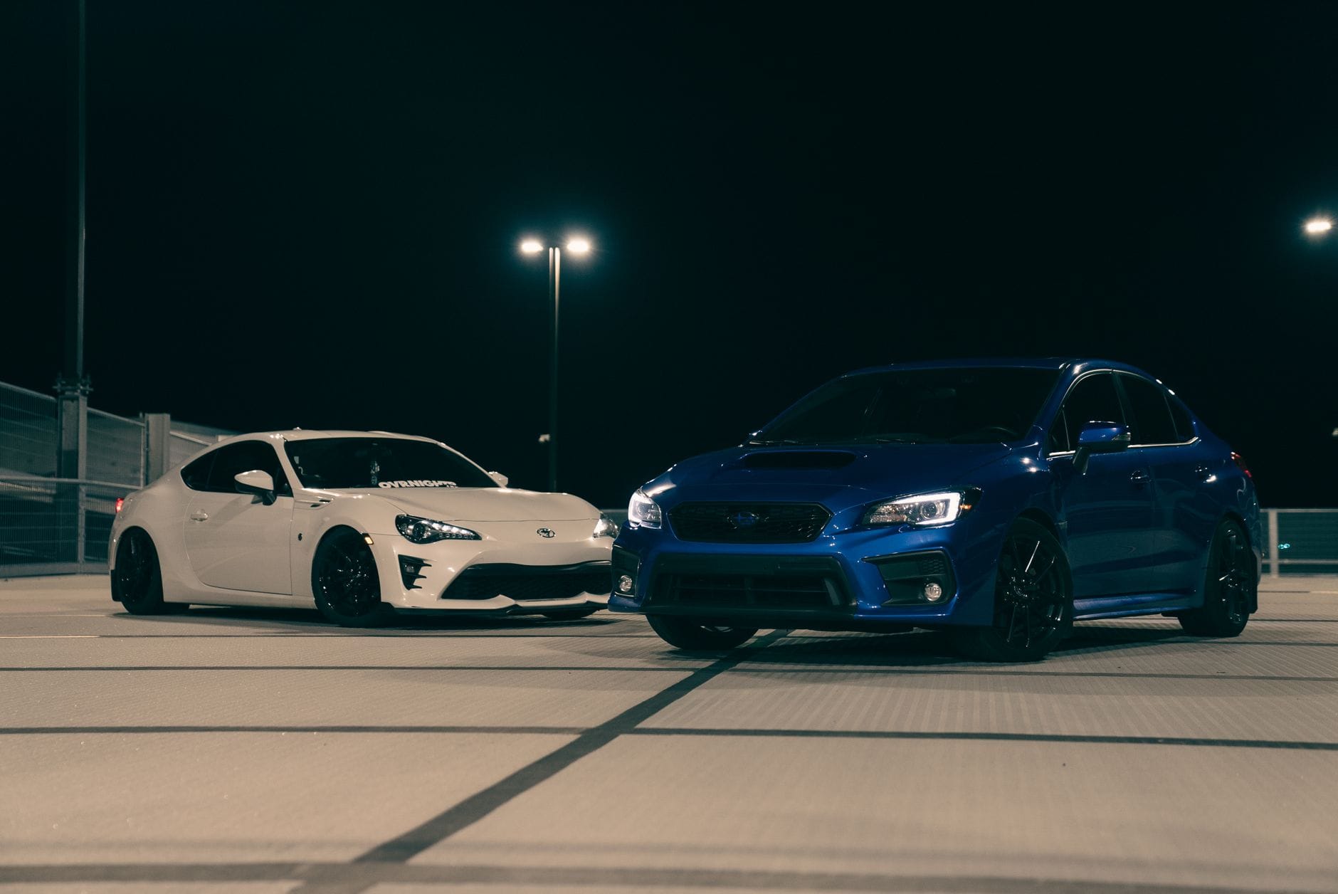 Białe i niebieskie Porsche sportowe zaparkowane nocą na dachu parkingu