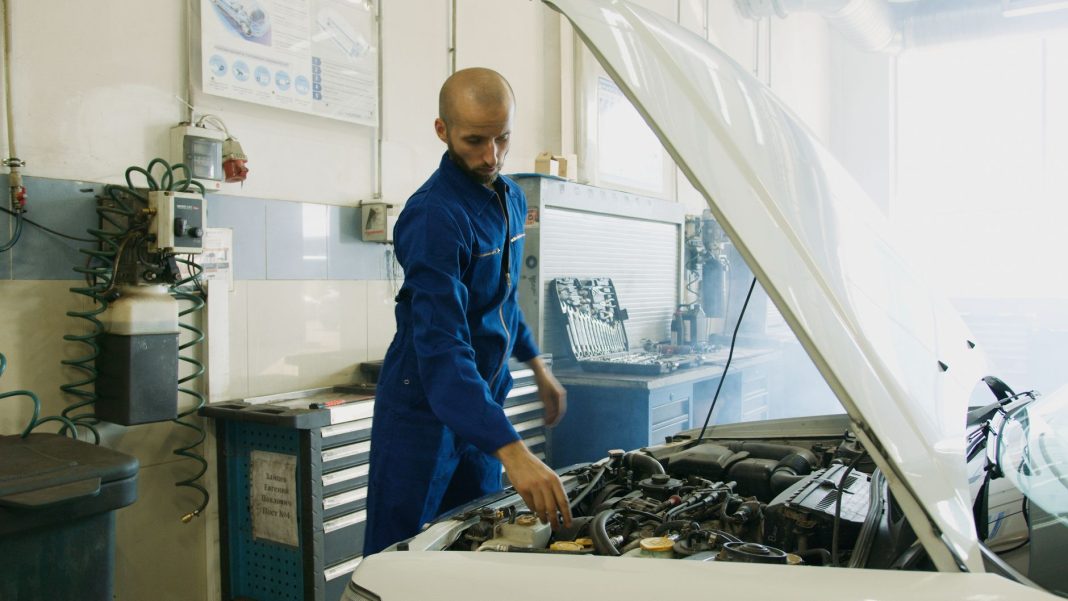 Mechanik w niebieskim kombinezonie sprawdza silnik Porsche w warsztacie Mechanik w niebieskim kombinezonie sprawdza silnik Porsche w warsztacie