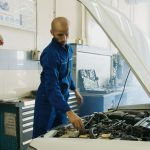 Mechanik w niebieskim kombinezonie sprawdza silnik Porsche w warsztacie